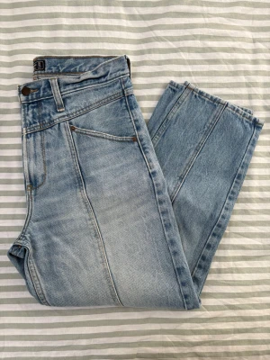 Abercrombie and Fitch barrel leg jeans regular length - Säljer ett par blå tvättade jeans från Abercrombie & Fitch med rörformade ben och en ok-detalj framtill, samt tydliga sömmar längs framsidan. Jeansen har hög midja, klassisk femfickdesign och bälteshällor. Tillverkade av tjock, icke-elastisk denim med en häftig vintage-känsla och en snygg tvätt. Mina favoritjeans när jag var yngre – ett riktigt häftigt och roligt par jeans för sommaren.
