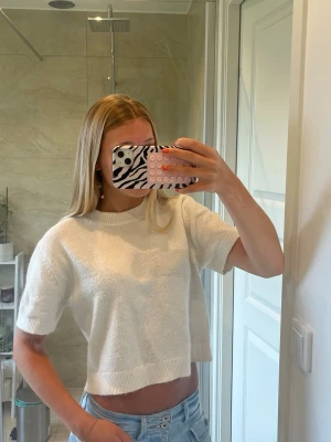 Vit stickad topp - Säljer en vit croppad stickad topp med korta ärmar och rund hals. Toppen har en relaxed fit och ribbade detaljer vid ärmslut, halsringning och nederkant. Knappt använd och säljer för att jag inte använder den.