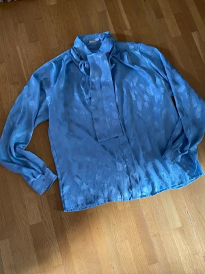 Ljusblå scarfblus i satinlook - Blus med knytband i halsen. Står strl 42 men tycker det är M