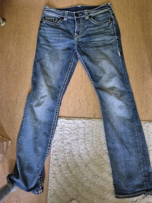 Blå jeans från True Religion - Säljer ett par blå jeans från True Religion med raka ben, stretch och tydliga kontrastsömmar. Jeansen har klassisk femficksmodell och dekorativa sömmar på bakfickorna. Materialet är denim i bomull med lätt slitna detaljer för en cool look.