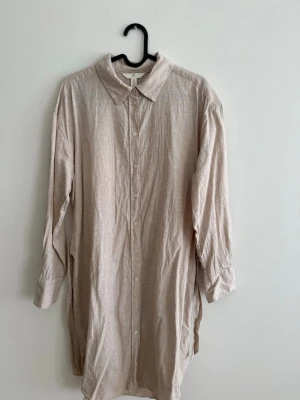 H&M Linneklänning - Linen Blend - Strl S - Fin och luftig linneklänning från H&M i en ljus beige ton. Tillverkad i linen blend som gör den sval och bekväm – perfekt till vår och sommar.  Klänningen har knäppning framtill och ett knytband i midjan som ger en fin silhuett. Kan även bäras öppen som en längre skjorta över t.ex. shorts eller jeans.  Märke: H&M Storlek: S Material: Linen blend Längd: ca 100 cm