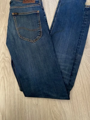 Mörkblå Lee slim jeans - Snygga mörkblå jeans i modellen Luke vilket är en slim jeans modell. Jeansen har en bakficka med dekorativ söm och en läderpatch i midjan. Perfekta till en avslappnad stil och tillverkade i slitstarkt denimtyg. Jeansen är typ oanvända endast provade ett par gånger dvs nyskick. Stl w28 l32. Hör av dig vid frågor!😊Pris kan diskuteras vid snabb affär!