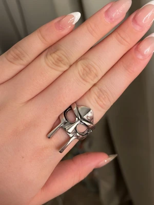 Silverfärgad ring med hjälmmotiv - Cool ring i silverfärgad metall formad som en hjälm, inspirerad av vikinga- eller riddartema. Ringen har öppningsbar baksida för justerbar storlek och detaljerade utskärningar framtill. Perfekt för dig som gillar unika och statement-accessoarer.