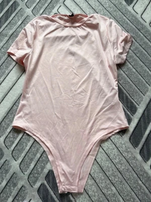 Ljusrosa kortärmad body - Söt ljusrosa body med korta ärmar och rund hals. Tillverkad i mjukt och stretchigt material som sitter skönt mot kroppen. Perfekt att styla med jeans eller kjol för en enkel och clean look.