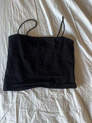 Svart ärmlös linnetopp - Säljer en enkel och stilren svart linnetopp med tunna axelband. Toppen har en rak passform och är perfekt att matcha med jeans eller kjol. Materialet känns mjukt och lätt mot huden.