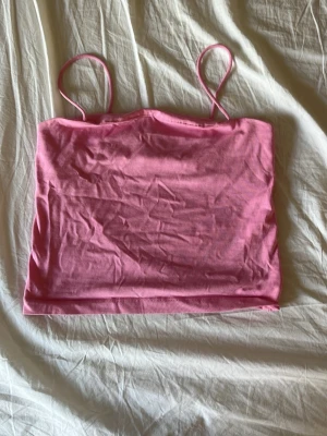 Rosa bandeau linnetopp - Säljer en söt rosa bandeau linnetopp med tunna axelband. Toppen är croppad och har en enkel, stilren design som passar perfekt till sommaren. Tillverkad i mjuk bomull för en bekväm känsla. Perfekt att matcha med jeans eller kjol!