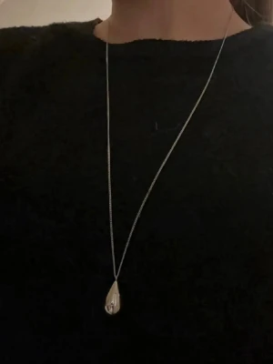 Silverfärgat halsband med droppe - Snyggt halsband med en lång, tunn kedja i silverfärg och ett droppformat hänge. 