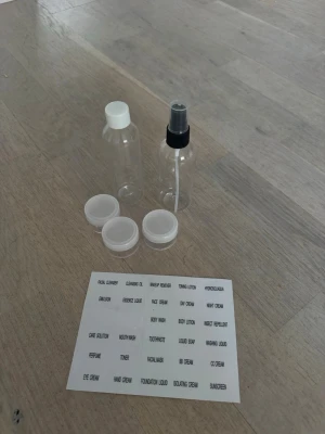 Resekit med tomma flaskor och burkar - Praktiskt resekit med två genomskinliga plastflaskor, en med spraypump och en med skruvlock, samt tre små plastburkar med vita lock.  Den vänstra är använd men självklart diskad, men verkar ha fått någon smäll någon gång så plasten är ej så jämn. Perfekt för att ta med hudvård eller schampo på resan. Medföljer även etiketter för enkel märkning.🌟