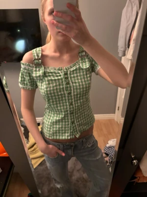 Grön rutig offshoulder blus - Söt grön och vit rutig blus med offshoulder och breda axelband. Toppen har knappar framtill och en figurnära passform. Passar mig som bär storlek S 