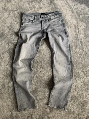 Ljusgrå slim jeans från Jack and Jones  - Säljer ett par ljusgrå jeans från Jack and Jones med rak passform och klassisk femficksdesign. Jeansen har en snygg tvättad look och är tillverkade i bomull med lite stretch för extra komfort. Perfekta för en avslappnad och trendig stil. Hör av dig vid minsta fundering och pris kan diskuteras! 🤩🙌