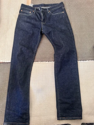 Mörkblå raka jeans i denim - Säljer ett par klassiska mörkblå jeans med rak passform och fem fickor. Jeansen har orangea sömmar och är tillverkade i kraftig denim. Perfekta för dig som gillar en tidlös och enkel stil.