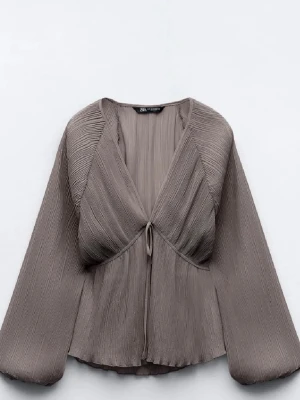 Blus från Zara - Trendig blus från Zara med djup V-ringning och knytning framtill. Blusen har vida, långa ärmar och ett flowy, transparent tyg som ger en luftig känsla. Perfekt för dig som gillar en avslappnad men ändå chic stil.