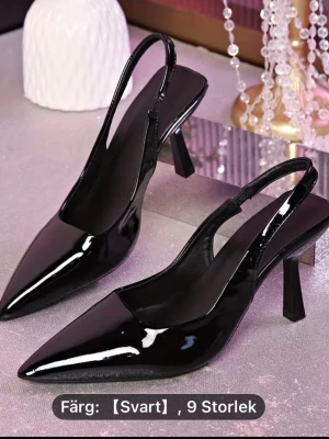 Svarta lackade slingback-pumps - Stilrena svarta pumps i lackat material med spetsig tå och öppen häl. Skorna har en elegant slingback-rem och smal klack som ger en trendig siluett. Perfekta för dig som vill ha en chic och modern look.