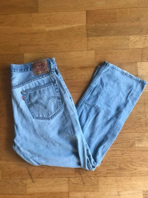 Levi's 505 ljusblå raka jeans - Klassiska ljusblå Levi's 505 jeans med rak passform och hög midja. Jeansen har fem fickor, Levi's ikoniska röda etikett på bakfickan och patch med logga i midjan. Tillverkade i slitstark denim av bomull, perfekta för en avslappnad och tidlös stil.