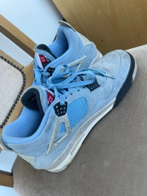 Jordan 4 University Blue sneakers - Snygga Jordan 4 University Blue sneakers i ljusblå mocka med vita och svarta detaljer. Skorna har meshpaneler på sidorna, svart yttersula och nummer 23 på plösen. Perfekta för dig som vill sticka ut med klassisk streetwearstil. För frågor har gärna av er. Storlek 46 passar även 45 