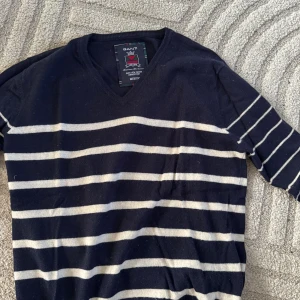 Marinblå randig tröja från GANT - Snygg marinblå tröja från GANT med vita horisontella ränder och V-ringning. Tröjan har långa ärmar och är tillverkad i mjukt material, perfekt för en avslappnad men stilren look.