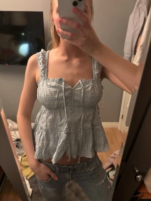 Blåvit rutig blus med volang - Söt blåvit rutig blus med volangdetaljer och breda axelband. Storlek S 