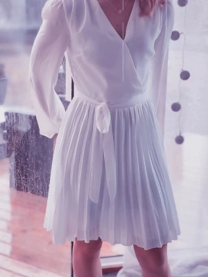 Vit omlottklänning med plisserad kjol - Säljer en söt vit omlottklänning från Bubbleroom, långärmad design, v-ringning och knytband i midjan. Kjolen är plisserad för en snygg och luftig look. Perfekt till avslutningen, studentfirande eller bara en fin sommarklänning. Använd endast en gång så I mycket fint skick.  Storlek 34