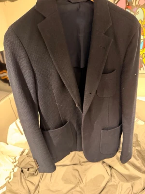 Mörkblå kavaj från j Lindeberg  - Stilren mörkblå kavaj från J Lindeberg med tre utanpåfickor och klassiska slag. Kavajen har en diskret struktur i tyget och är helfodrad med matchande blått foder, perfekt som overshirt eller för en riktigt fet outfit. Nypris 2699:)