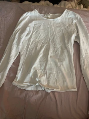 Vit långärmad topp från H&M - En enkel och stilren vit långärmad topp från H&M. Tillverkad i mjuk bomull med rund halsringning och normal passform. Perfekt att matcha med jeans eller kjol för en clean look.
