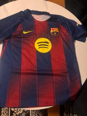FC Barcelona matchtröja Nike blå/röd - Säljer en FC Barcelona matchtröja från Nike i blått och rött med gula detaljer. Tröjan har klubbmärke, Nike-logga och Spotify-logga på bröstet. Klassisk design med vertikala ränder och rund hals, tillverkad i lätt och ventilerande material.