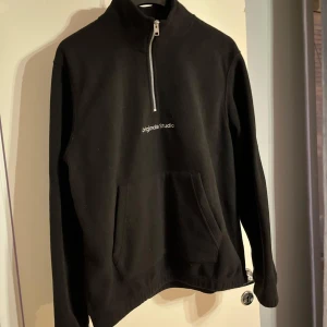 Svart sweatshirt från Originals Studio - Från Originals Studio med halv dragkedja framtill och en stor magficka. Minimalistisk design med liten vit logga på bröstet. Tillverkad i mjukt material och har en hög krage för extra stilpoäng.