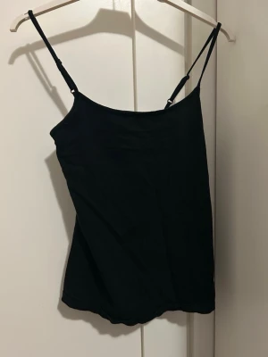 Svart linnetopp från Primark - En enkel och stilren svart linnetopp från Primark med tunna justerbara axelband. Toppen är ärmlös och har en smal passform som sitter snyggt på kroppen. Perfekt att matcha med jeans eller kjol för en clean look. Linnet är i storlek S.