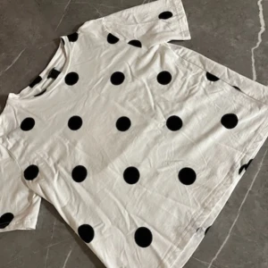 Vit t-shirt med svarta prickar - Säljer en vit t-shirt med stora svarta prickar. T-shirten har korta ärmar och en avslappnad passform. Perfekt för dig som gillar lekfulla mönster och vill sticka ut lite extra.