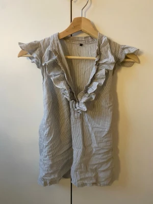 Randig blus med volangkant - Söt blus med smala blå och vita ränder, djup v-ringning och volangdetaljer längs halsen. Kortärmad modell i lätt och luftig bomull, perfekt för en avslappnad och trendig look. Passar till både jeans och kjol. skulle säga att den passar som storlek S-M men står 8 i den!!