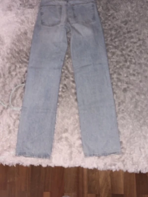 Ljusblå raka jeans - Säljer ett par ljusblå jeans med raka ben och klassisk femficksdesign. Jeansen har en enkel och tidlös look, perfekta till många olika stilar. Materialet är denim i bomull. Passar dig som gillar en avslappnad vibe.