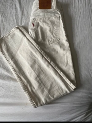 Vita raka jeans från Levi's - Säljer ett par vita jeans från Levi's med klassisk rak passform och femficksmodell. Jeansen har en snygg läderpatch bak i midjan och är tillverkade i kraftig bomullsdenim. Perfekta för dig som vill ha en clean och tidlös look.