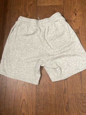 Ljusgrå mjukisshorts med snörning - Mysiga ljusgrå shorts i mjuk bomullsblandning med elastisk midja och snörning. Klassisk passform med två sidofickor, perfekta för chill dagar eller träning. Enkel och stilren design utan synliga loggor eller mönster.