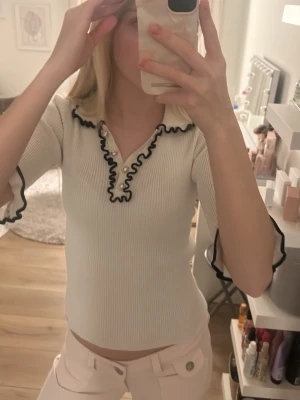 Vit blus med svarta detaljer - Riktigt snygg tröja. Tyvärr är det hål i tröjan på baksidan(kolla bilden), är man duktig på att sy är detta perfekt för dig!