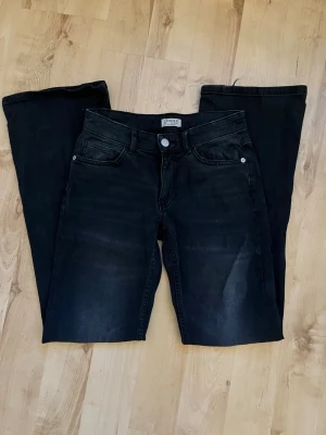 Svarta bootcut jeans från Lindex - Snygga svarta bootcut jeans från Lindex med klassisk femficksmodell och lätt tvättade detaljer framtill. Jeansen har låg midja och utsvängda ben.