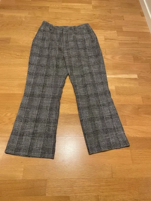 Rutiga grå kostymbyxor - Snygga kostymbyxor i grått med svartvitt rutmönster. Byxorna har rak passform och klassisk midja. Perfekta för dig som vill ha en stilren men trendig look. Materialet känns mjukt och bekvämt, troligen en blandning av polyester och viskos.