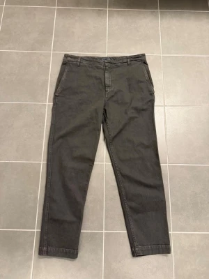 Mörkgrå chinos med raka ben från Dondup, stl 32 - Snygga mörkgrå chinos med raka ben och klassisk passform. Byxorna har sidofickor, en bakficka med knapp och hällor för bälte. Tillverkade i ett mjukt bomullstyg som ger en skön känsla och stilren look.