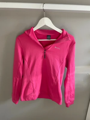 Rosa träningströja från Odlo - Snygg rosa långärmad träningströja från Odlo med halv dragkedja framtill och hög krage. Perfekt för löpning eller gym. Tillverkad i mjukt funktionsmaterial som andas. Diskret logga på bröstet och figurnära passform.