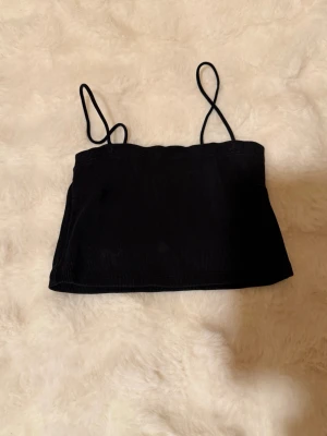 Svart ribbad linnetopp Gina Tricot - Snygg svart ribbad linnetopp från Gina Tricot med tunna axelband. Toppen har en croppad passform och är perfekt för varma dagar eller som layering-piece. Enkel och stilren design som passar till det mesta. Passar xs/s