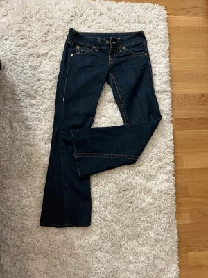Mörkblå bootcu  true religion jeans - Snygga mörkblå bootcut jeans från true religion med klassiska kontrastsömmar och fem fickor. Jeansen har låg midja och är tillverkade i ett mjukt denimtyg som sitter skönt. Perfekta för dig som gillar en tidlös och clean look.