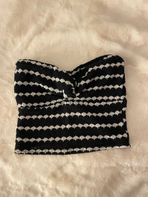 Randig svartvit bandeau tubtopp - Säljer en snygg bandeau tubtopp i svart och vitt med horisontella ränder. Toppen har twistad detalj framtill och är tillverkad i ett stretchigt, mjukt material som känns bekvämt mot huden. Perfekt för sommaren och enkel att styla till olika outfits.