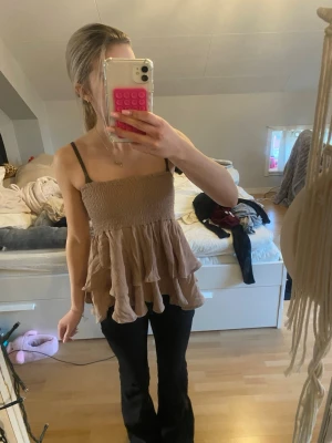 Beige volang topp med volang - Säljer en beige topp volang nedtill. Toppen har en smockad överdel och är ärmlös, vilket ger en luftig och söt look. Perfekt för dig som gillar en somrig look. Är i storlek 10-11 men passar mig som bär XS