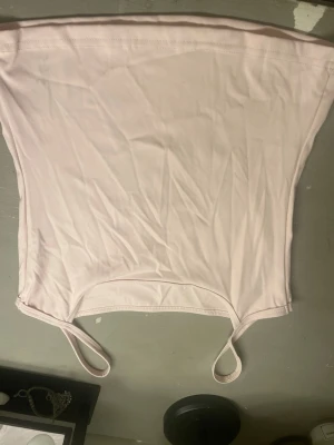 Ljusrosa bandeau tubtopp - Säljer en ljusrosa bandeau tubtopp med smala axelband. Toppen är enkel och stilren, perfekt att matcha med olika outfits. Tillverkad i mjuk polyester som känns skön mot huden.