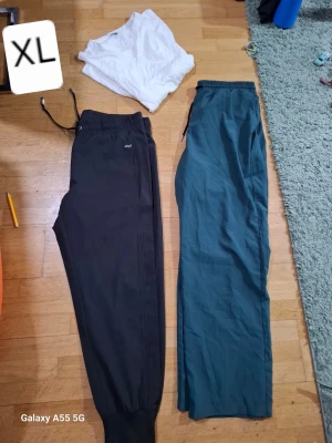 Två par mjukisbyxor XL - Säljer två par mjukisbyxor i storlek XL. Ena paret är svart med resår och dragsko i midjan samt muddar vid benslut, från 4F. Det andra paret är mörkgrönt med resår i midjan och raka ben. Perfekta för chill eller träning.