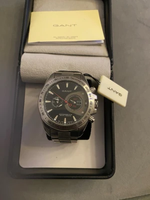 GANT herrklocka i silver - Stilren herrklocka från GANT med svart urtavla, silverfärgade detaljer och länkarmband i metall. Klockan har kronograf, tachymeter och datumvisning. Perfekt accessoar för dig som gillar klassisk och sportig stil. Ny batteri 