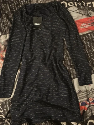 Mörkblå långärmad klänning ONLY - Mörkblå kortklänning från ONLY med diskret glittrigt mönster. Klänningen har lång ärm och en kroppsnära passform. Perfekt för dig som vill ha en enkel men snygg look med lite extra detalj.
