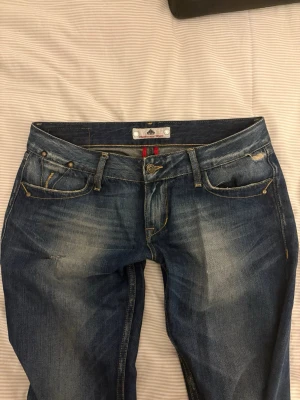 Blåa jeans från Fornarina  - Säljer ett par blåa jeans från Fornarina med slitna detaljer och snygg tvätt. Jeansen har fem fickor, kontrastsömmar och unika bakfickor med broderade detaljer. Klassisk knappgylf och skön passform. 