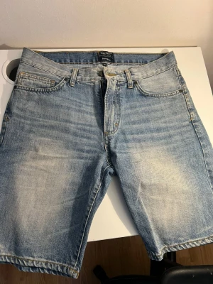 Ljusblå jeansshorts från East West - Säljer ett par ljusblå jeansshorts från East West, modell Bowery. Klassisk femficksdesign, bälteshällor och dragkedja. Shortsen har en avslappnad passform och är tillverkade i bomull med snygg tvättad look.