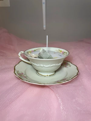 Doftljus i vaniljdoft i en tekopp med fat och blommig design  - Det här ljuset är gjort av återanvändbara material. Tekoppen är köpt secondhand och stearinet är från kyrkor som tänkte slänga det. Det här ljuset har en svag doft utav vanilj, så känsliga även kan använda det. Det här ljuset har även torkade blommor på som dekoration. 