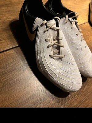 Fotbollsskor Nike - Fotbollsskor Phantom GX från Nike i storlek 42! Svarta och vita med gulddetaljer!