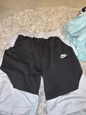 Svarta och grå shorts från Nike - Säljer ett par sportiga shorts från Nike i svart och grått med elastisk midja och logga på vänster ben. Perfekta för träning eller chill dagar. Sköna och lätta att röra sig i.